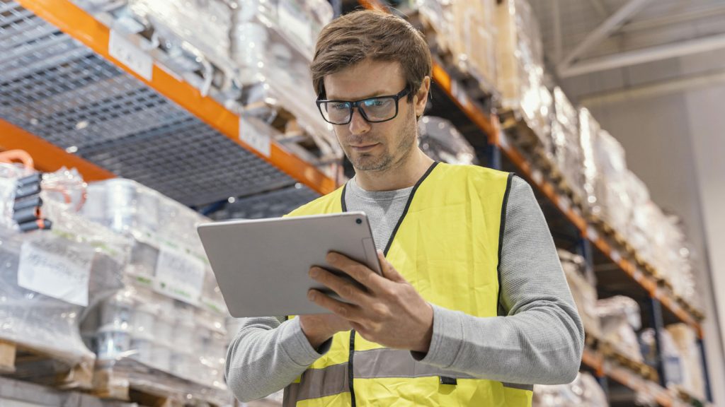 Man die werkt op een tablet in een modern magazijn, met digitale logistieke hulpmiddelen