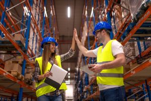 Lachende vrouwelijke magazijnmedewerker met veiligheidshelm en hesje in logistiek magazijn – NFA Recruitment Venlo vacatures.